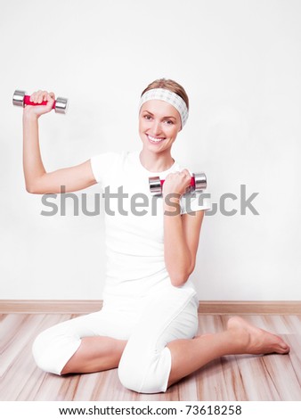 beautiful young woman working out with two dumbbells at home