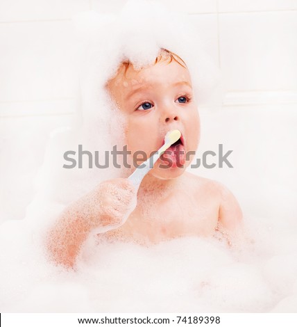 cute one year old baby taking a bath with foam and brushing teeth