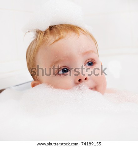 cute one year old boy taking a relaxing bath with foam