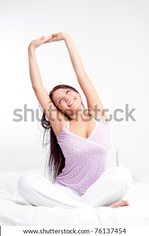 pretty smiling girl sitting on the bed at home waking up and stretching