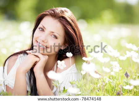 beautiful young brunette woman  on the  meadow with white flowers  on a warm summer day