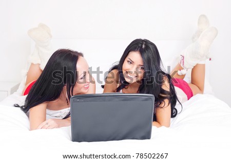 two happy laughing girls with  a laptop on the bed at home
