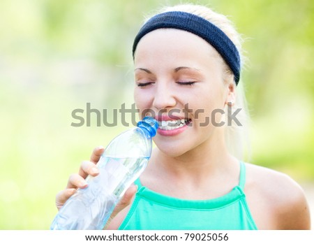beautiful young blond sporty woman running in the park on a warm summer day and drinking water