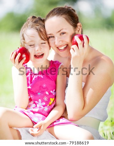 beautiful young mother and her daughter eating apples in the park on a sunny summer day (focus on the woman)
