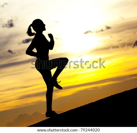 Silhouette of a beautiful woman running up the hill against yellow sky with clouds at sunset