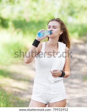 beautiful young  sporty woman running in the park on a warm summer day and drinking water