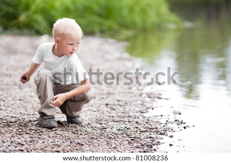 cute five year old boy throwing stones to the water outdoor on a summer day