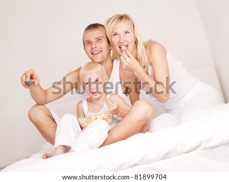 happy family; mother ,father and their son watching TV and eating popcorn in  bed at home