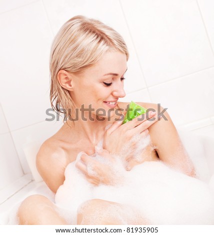 beautiful young blond woman taking a bath with foam and using a homemade glycerin soap