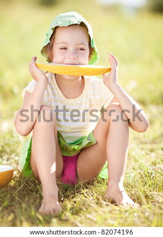 cute happy  little girl eating melon on the grass in summertime