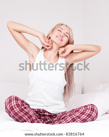 beautiful young blond woman waking up and stretching on the bed at home