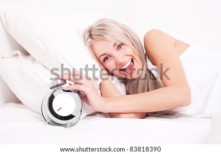 happy positive  young blond woman waking up and switching off the alarm clock