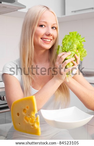 beautiful young blond woman with salad and cheese in the kitchen at home