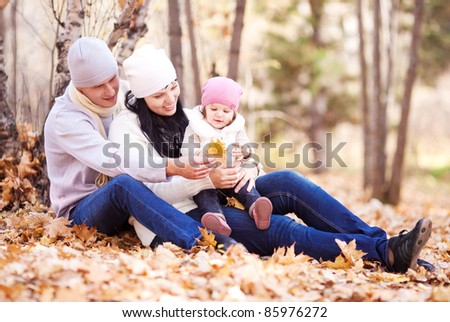 happy young family with their daughter spending time outdoor in the autumn park (focus on the woman)