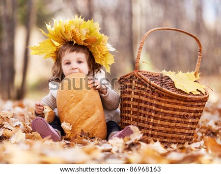 cute baby girl having a picnic, sitting on the grass in the autumn park and eating a long loaf
