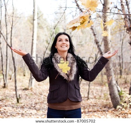 beautiful young brunette woman catching the maple leaves  falling on her  in the autumn park