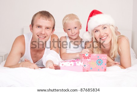happy family celebrating Christmas and opening presents: mother ,father and their son on the bed at home