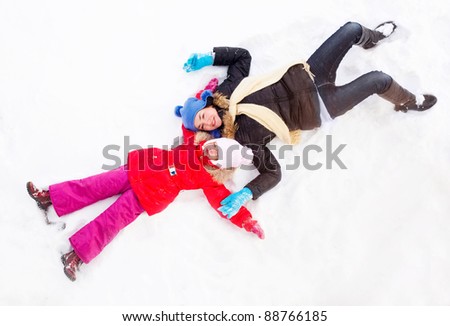 happy  family; mother and daughter making snow angels outdoor on a winter day
