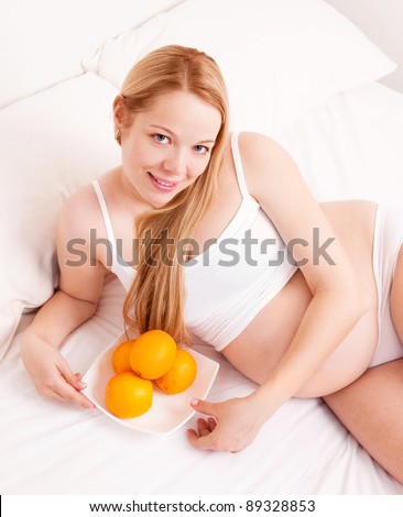 beautiful young pregnant woman  with oranges in bed at home smiling