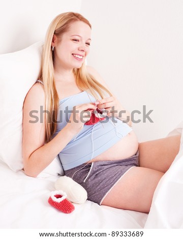 beautiful young pregnant woman  knitting baby\'s bootees in bed at home smiling