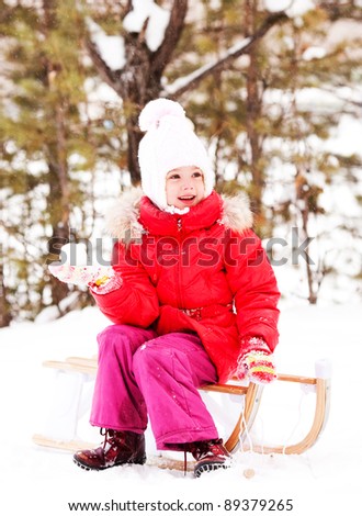 happy little girl sitting on the sledge and throwing a snowball,  outdoor in the park on a winter day
