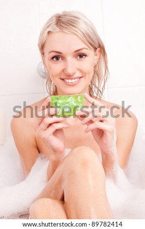beautiful young blond woman taking a bath with foam and using a  glycerin soap