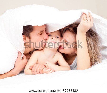 happy family; mother ,father and their baby under the blanket on the bed at home (focus on the woman)