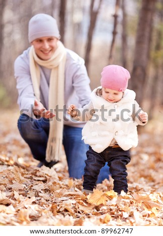 happy young father playing with his daughter  in the autumn park (focus on the child, the man is at a distance)