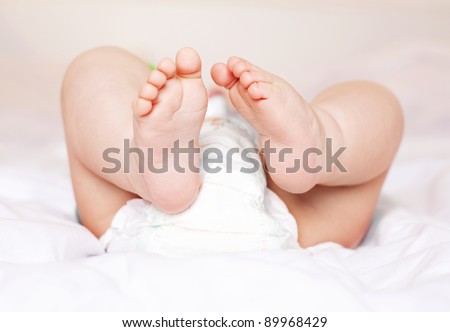 feet of a six months old baby wearing diapers lying on the bed at home