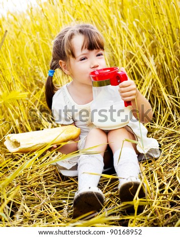 happy cute little girl having a picnic in the wheat field drinking milk and eating a long loaf