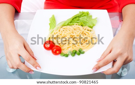 hands of a woman eating spaghetti with tomatoes, salad and peas