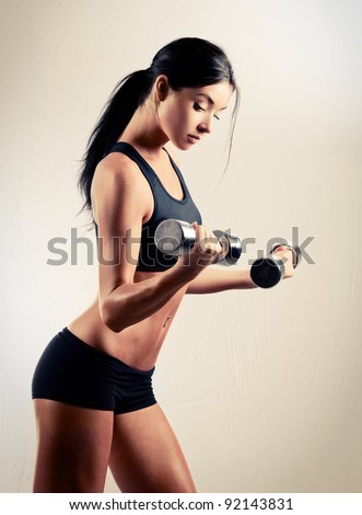 studio portrait of a beautiful sporty muscular woman working out with two dumbbells
