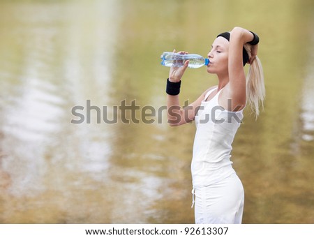 beautiful young blond sporty woman jogging in the park on a warm summer day and drinking water
