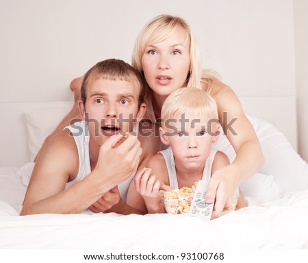 happy family: mother ,father and their son watching TV and eating popcorn on the bed at home