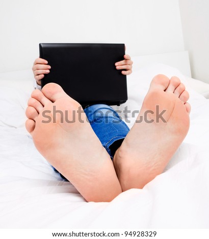 humorous portrait of a student with the laptop in bed at home, focus on the feet