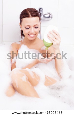 beautiful young brunette woman taking a relaxing bath with foam and using shampoo into her palm