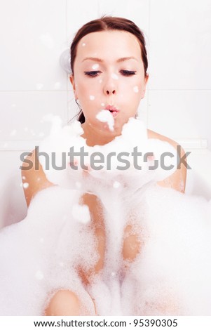 beautiful young brunette woman taking a relaxing bath and blowing on foam