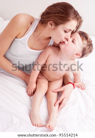 happy young mother and her two year old son embracing and kissing  in bed at home
