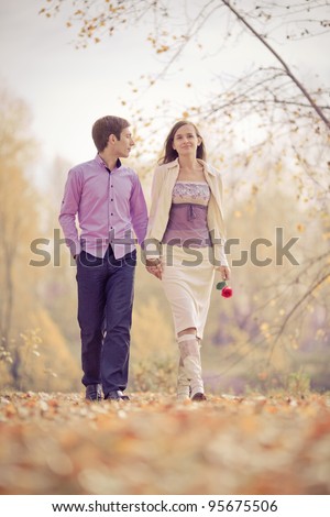 low contrast portrait of a happy loving couple walking and holding hands outdoor in the autumn park (focus on the man)
