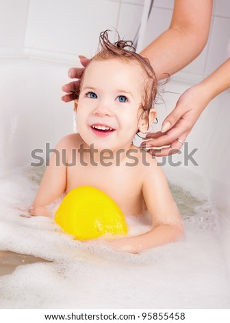 mother washing her baby in the bath with foam