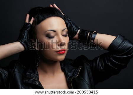 woman with bright makeup, wearing leather, against dark studio background