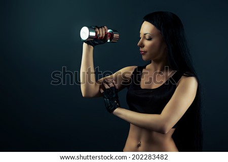 beautiful sporty young woman with a dumbbell against dark studio background