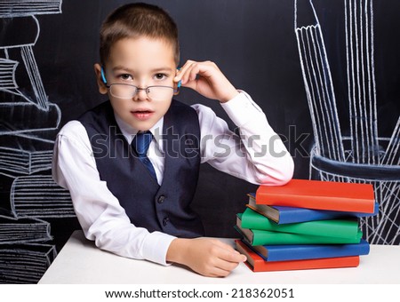 serious seven year old school boy sitting by the table with books