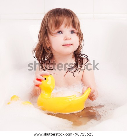 cute one year old girl taking a bath with foam and playing with a toy duck