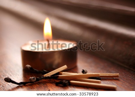 Tea-light candle on a wooden altar surrounded by burnt matches