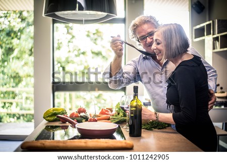 Senior couple cooking healthy food and drinking red wine at house kitchen