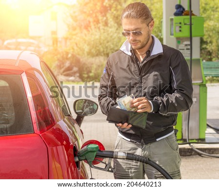 Young man filling car at gasoline tank while counting money