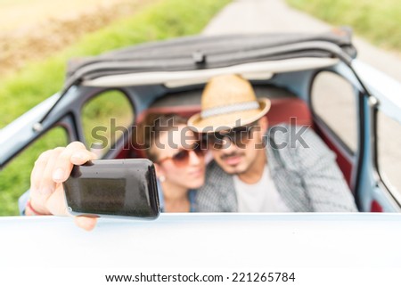 Happy couple in a vintage car.Two friends taking a selfie while driving through countryside.