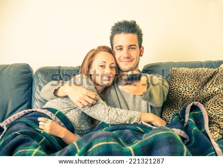 Happy couple watching television on the couch - family,recreation,leisure,togetherness concept