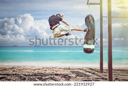 martial artist in action. performing a flying kick on a boxing bag on the beach. idyllic atmosphere